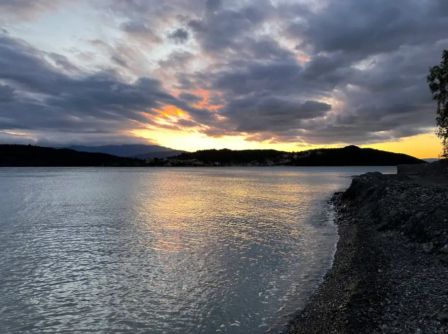 Das Bild von einfach-herumgurken zeigt einen Sonnenuntergang in Griechenland. Das Wohnmobil steht am Meer und man Blickt Richtung Gebirge, hinter welchem die Sonne verschwindet.