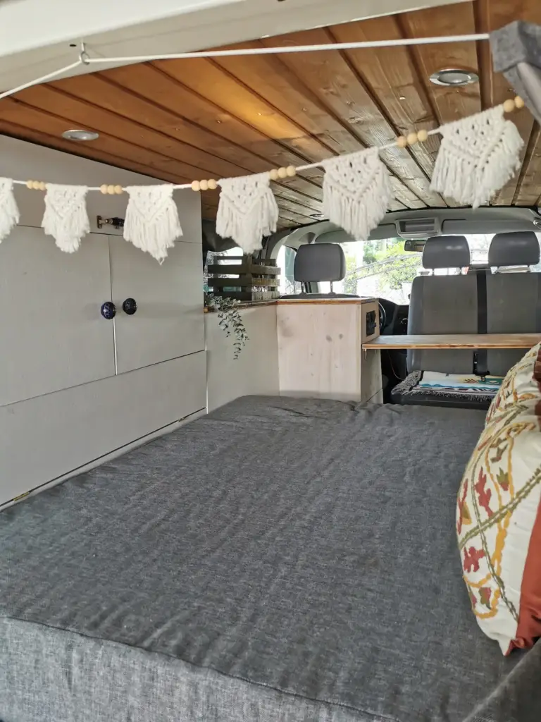Blick von hinten in den Van - Blick über das Bett, auf die Regale und den Tisch.